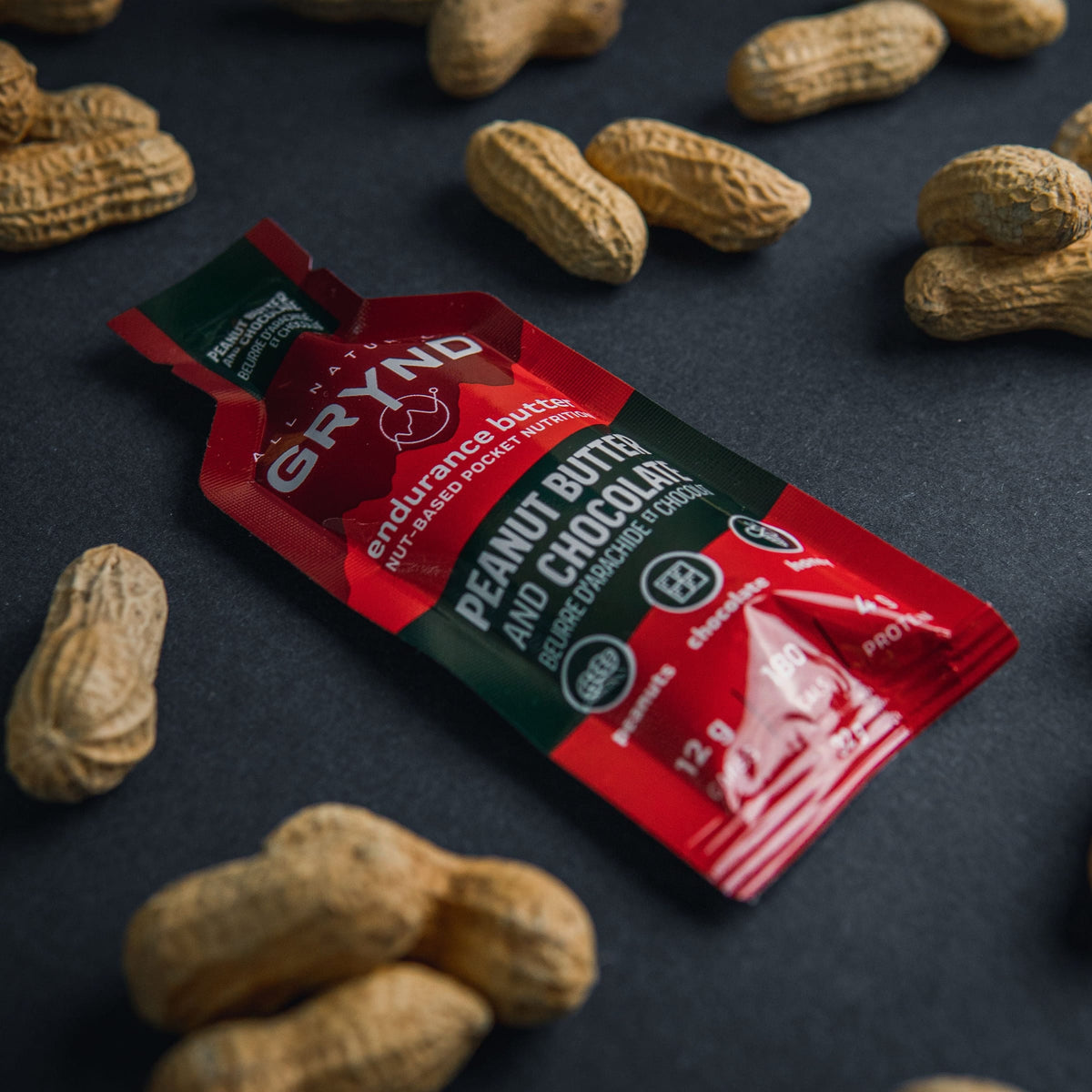 Grynd peanut butter and chocolate bar packaging surrounded by peanuts on a dark surface